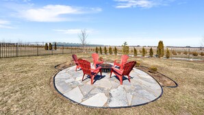 A patio with red Adirondack chairs and a stone fire pit, surrounded by a stone deck and a metal fence.