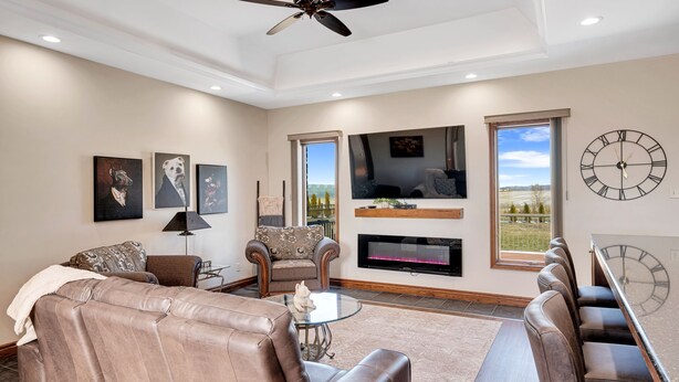 A spacious living room with a sofa, armchairs, a glass coffee table, a fireplace, a TV, and a large clock on the wall.