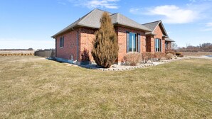 A brick house with a gabled roof, a large evergreen tree, and a well-maintained lawn.