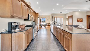 A modern kitchen with wooden cabinets, a central island, and a dining area in the background.