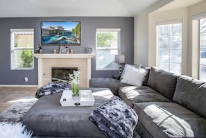 A modern living room with a gray sofa, a fireplace, and a large TV mounted above it.