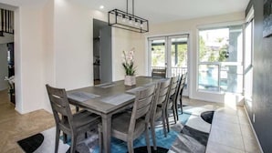 Un coin repas comprenant une table rectangulaire, six chaises, un luminaire suspendu et une plante en pot.