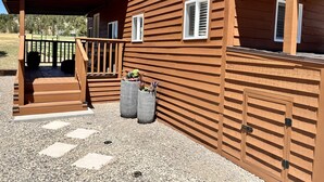 A wooden cabin with a covered porch, two potted plants, and a gravel pathway. - The Luxe Tiny Cottage  (Mayhill)