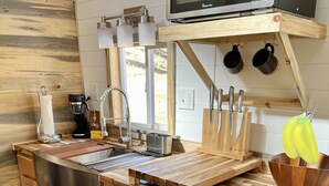 A modern kitchen with wooden cabinetry, a stainless steel sink, a coffee maker, and a microwave. - The Luxe Tiny Cottage  (Mayhill)