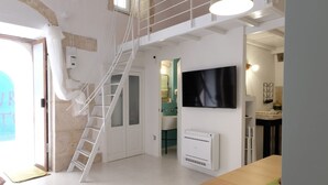 Een kamer met een witte trap, een flatscreen televisie, een witte radiator en een houten tafel.