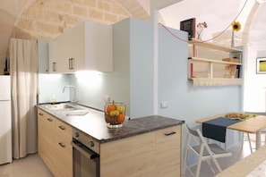 A compact kitchen with a marble countertop, a fruit bowl, and a dining area with a table and chairs.