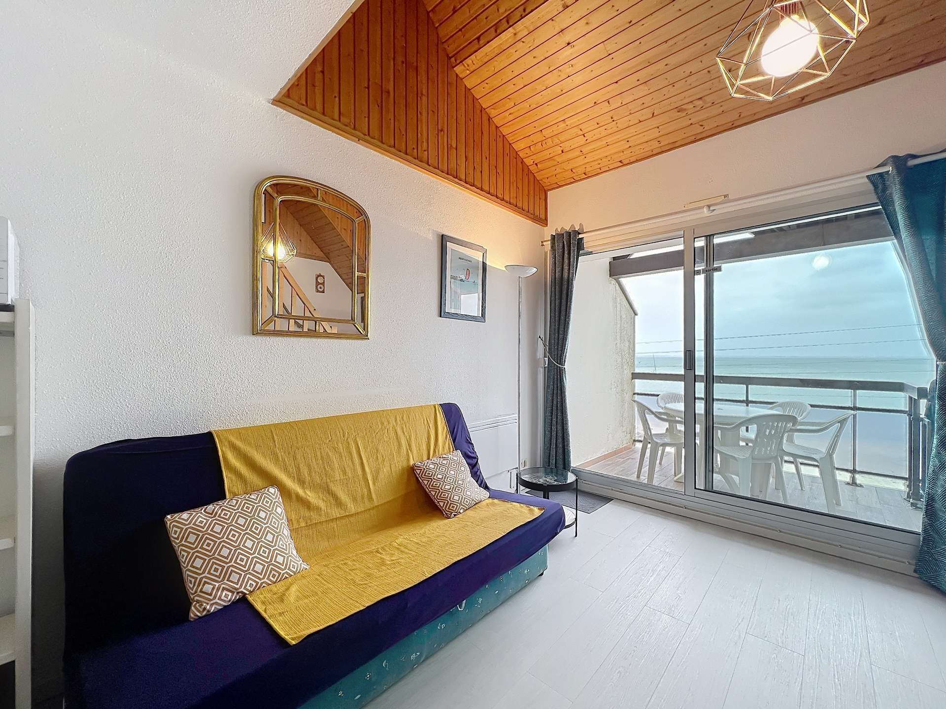 A room with a sofa, a framed mirror, and a view of the sea through a glass door.