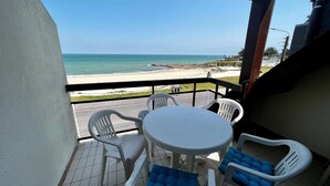 Ein Balkon mit Blick auf den Strand, ein runder Tisch und zwei Stühle mit blauen Kissen.