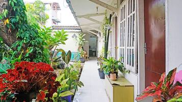 A covered corridor with potted plants, a wooden door, and a tiled floor.