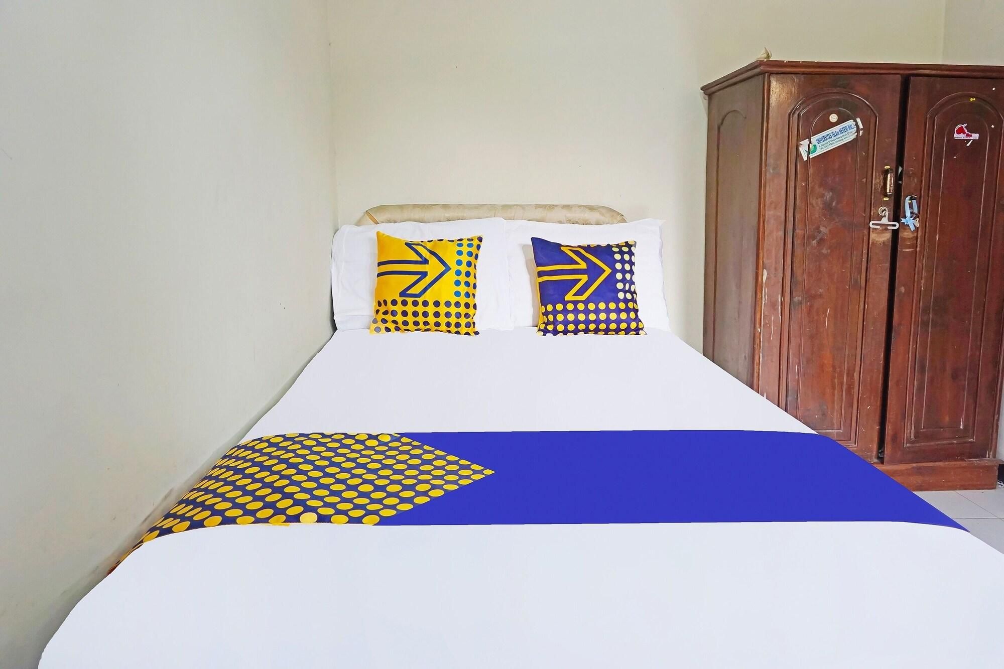A bed with a blue and yellow patterned bedspread, two pillows with similar designs, and a wooden wardrobe in the background.