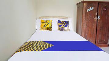 A bed with a blue and yellow patterned bedspread, two pillows with similar designs, and a wooden wardrobe in the background.