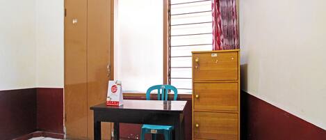 A room with a wooden cabinet, a table, a chair, and a window with blinds.