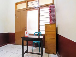 Ein Zimmer mit einem Holzkasten, einem Tisch mit Stuhl und einem Fenster mit Jalousien.