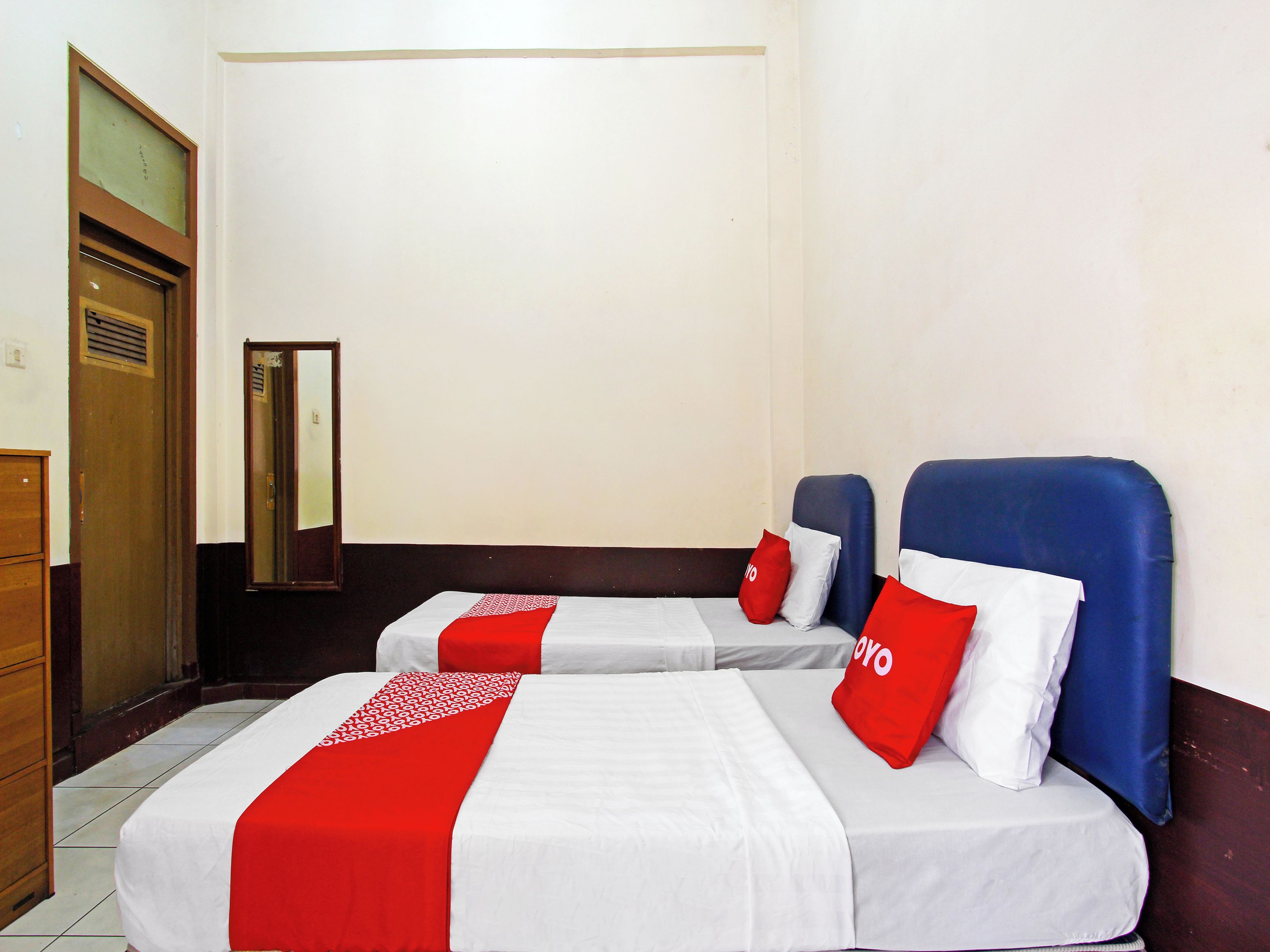 Habitación de hotel con dos camas, cada una con una colcha roja y blanca, y un espejo en la pared.