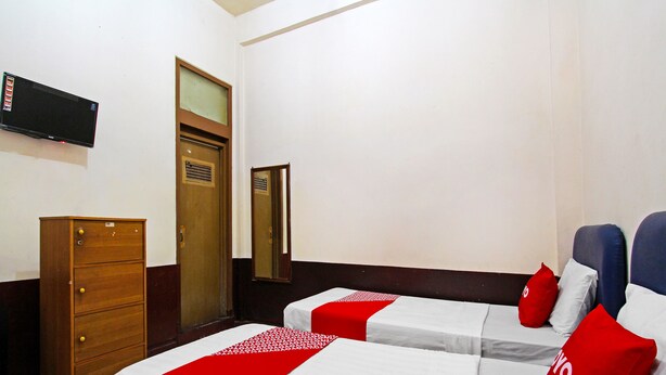 A hotel room with two beds, a wooden dresser, a television on the wall, and a mirror.