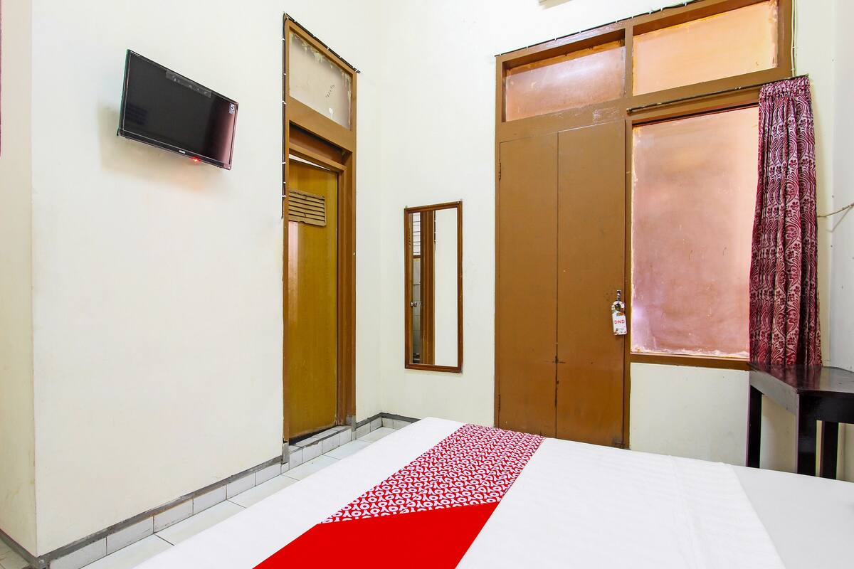 A hotel room with a bed, a television, a wardrobe, and a window with curtains.