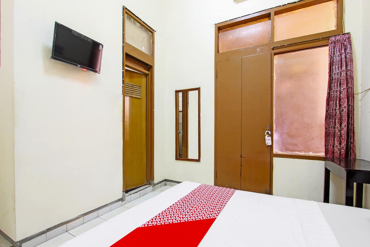 A hotel room with a bed, a television, a wardrobe, and a window with curtains.