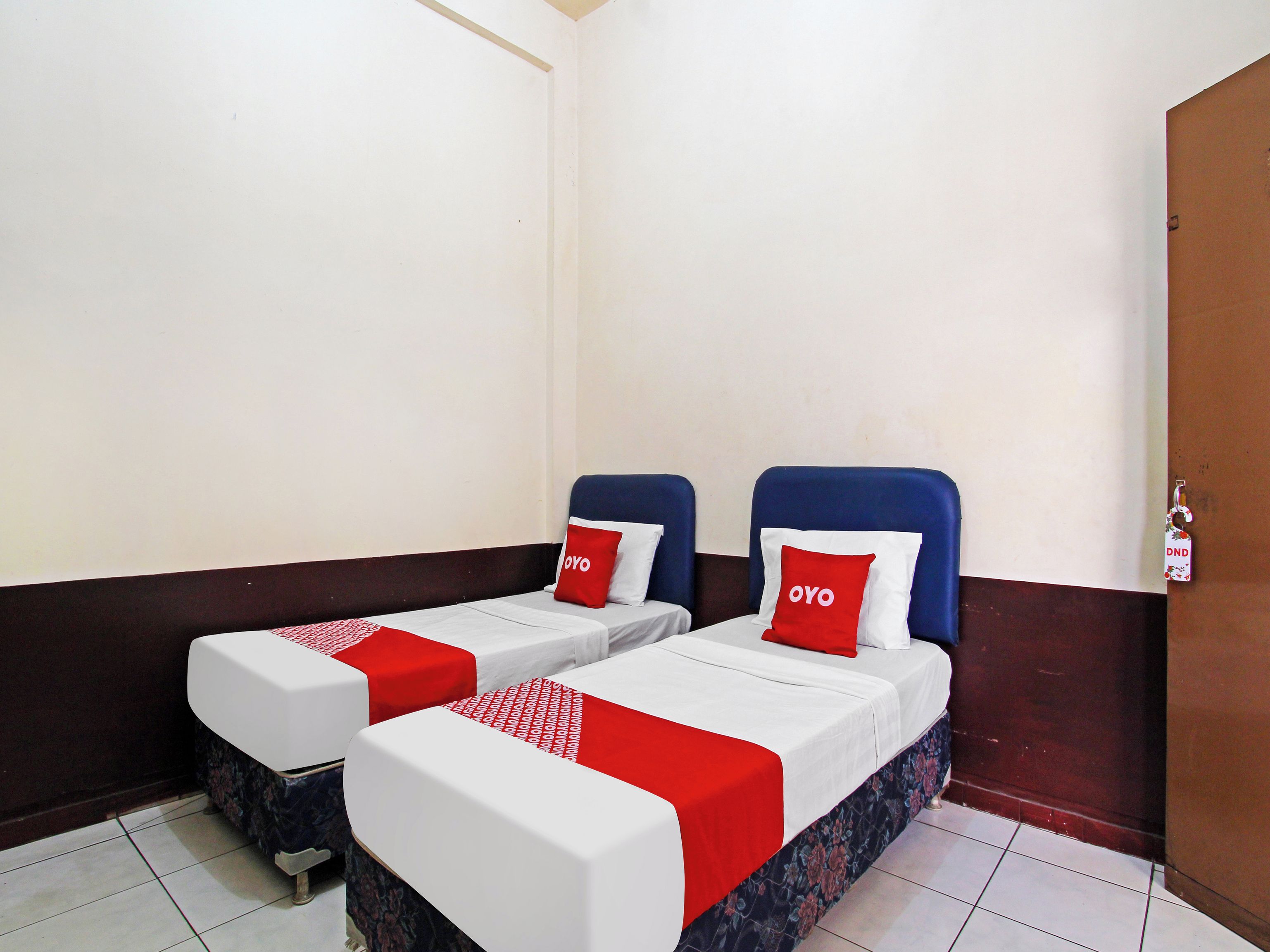 A hotel room with two beds, each with a red and white bedspread and pillows, and a wooden door.