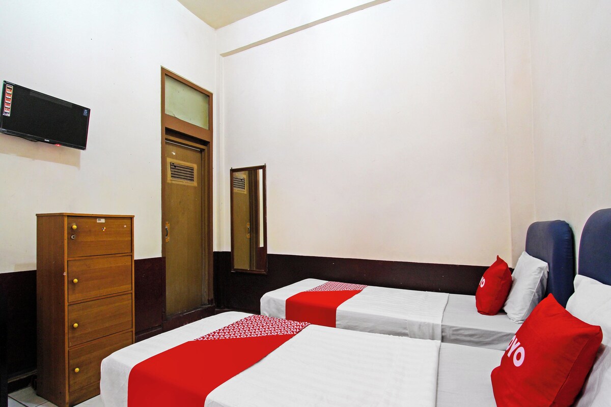 Ein Hotelzimmer mit zwei Betten, einem Holzkoffer, einem an der Wand befestigten Fernseher und einem Spiegel.
