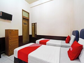 Ein Hotelzimmer mit zwei Betten, einem Holzkoffer, einem an der Wand befestigten Fernseher und einem Spiegel.