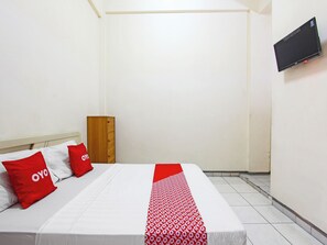 Een hotelkamer met een bed, een houten garderobe, een flatscreen televisie aan de muur en een betegelde vloer.