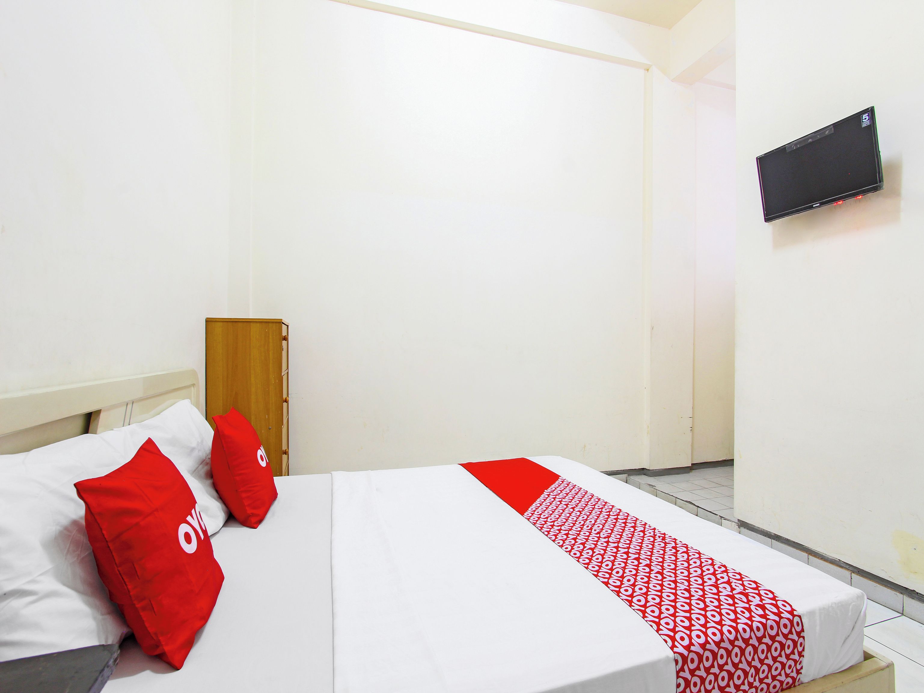 A single bed with a white and red bedspread, two red pillows, and a wooden headboard.