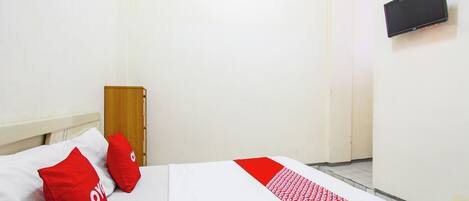 A single bed with a white and red bedspread, two red pillows, and a wooden headboard.