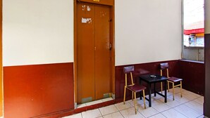 A room with a brown door marked "211", a small table with two chairs, and a window with a red awning.