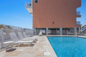 A rooftop pool area with white lounge chairs and a clear blue pool. - GULF-FRONT CONDO, OUTDOOR POOL, FAMILY FRIENDLY! (Gulf Shores)