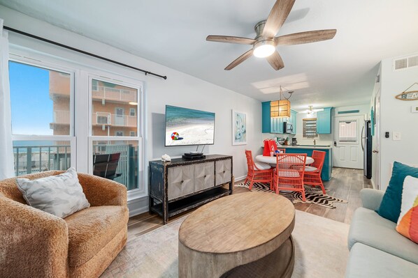 A living room with a sofa, coffee table, and a TV on a cabinet. There is a ceiling fan and a view of the balcony. - GULF-FRONT CONDO, OUTDOOR POOL, FAMILY FRIENDLY! (Gulf Shores)