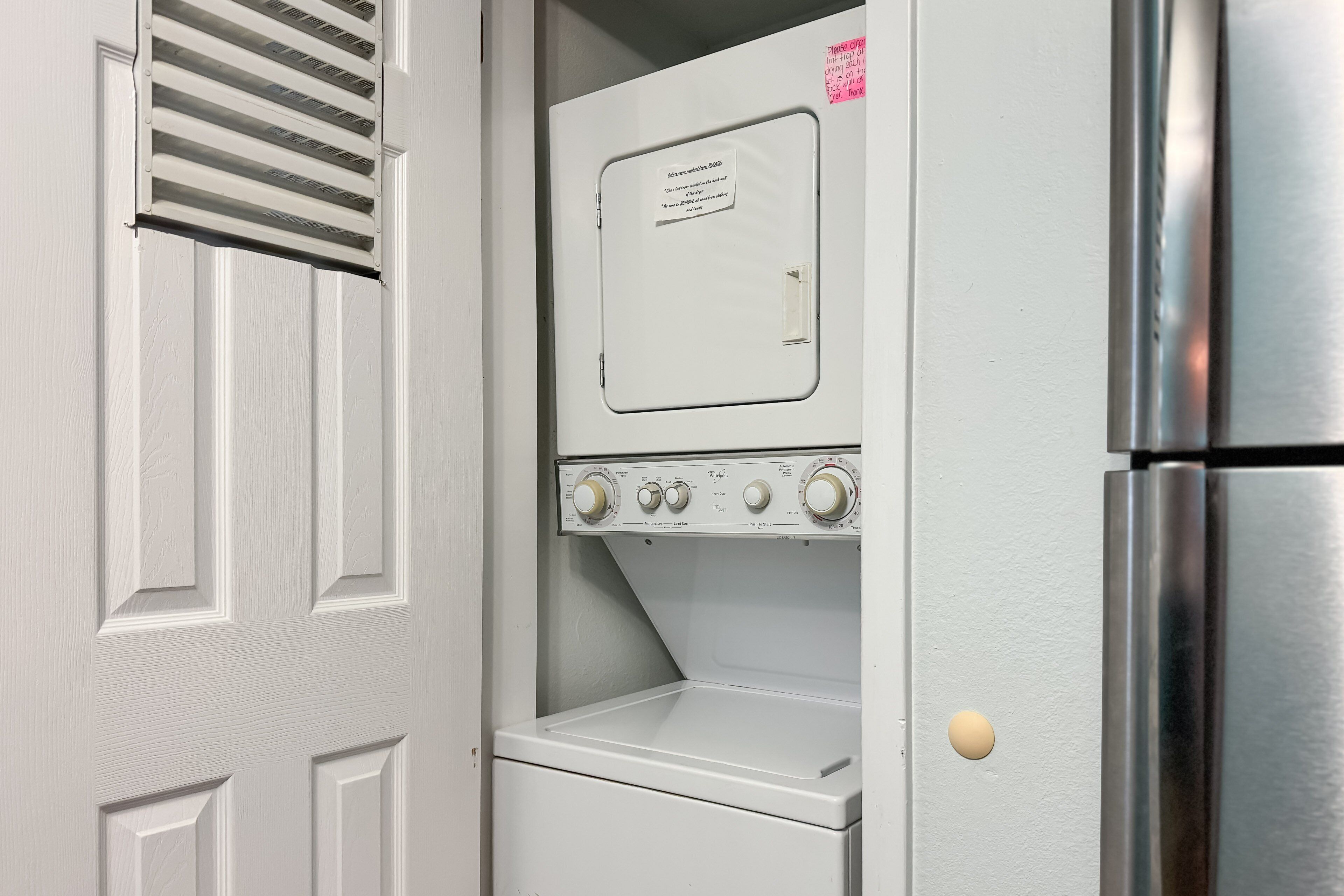 A compact laundry room with a built-in washer and dryer, a vent above the dryer, and a stainless steel refrigerator to the right.