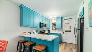 Une cuisine avec des meubles de couleur turquoise, un îlot central blanc doté de tabourets, un four à micro-ondes et un réfrigérateur.
