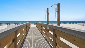 Une jetée en bois menant à une plage où se trouvent des parasols et des chaises longues.