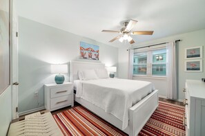 A bedroom with a bed, nightstands, a ceiling fan, a window with blinds, and a wall-mounted artwork. - GULF-FRONT CONDO, OUTDOOR POOL, FAMILY FRIENDLY! (Gulf Shores)