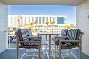 A balcony with two striped chairs and a small round table, overlooking a building with multiple windows and palm trees.