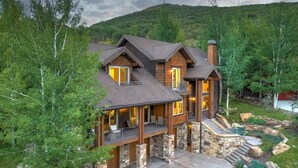 Una cabaña grande de dos pisos construida con troncos, con base de piedra, varios balcones y una chimenea de piedra.