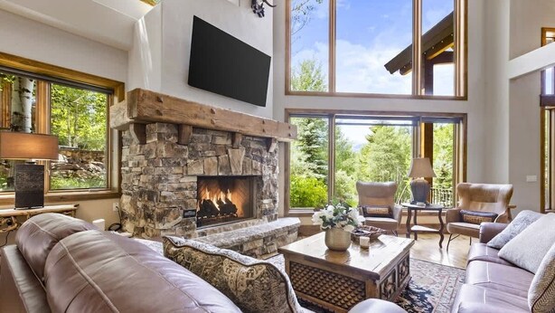 Amplia sala de estar con chimenea de piedra, sofás de cuero y ventanas grandes con vistas al exterior.