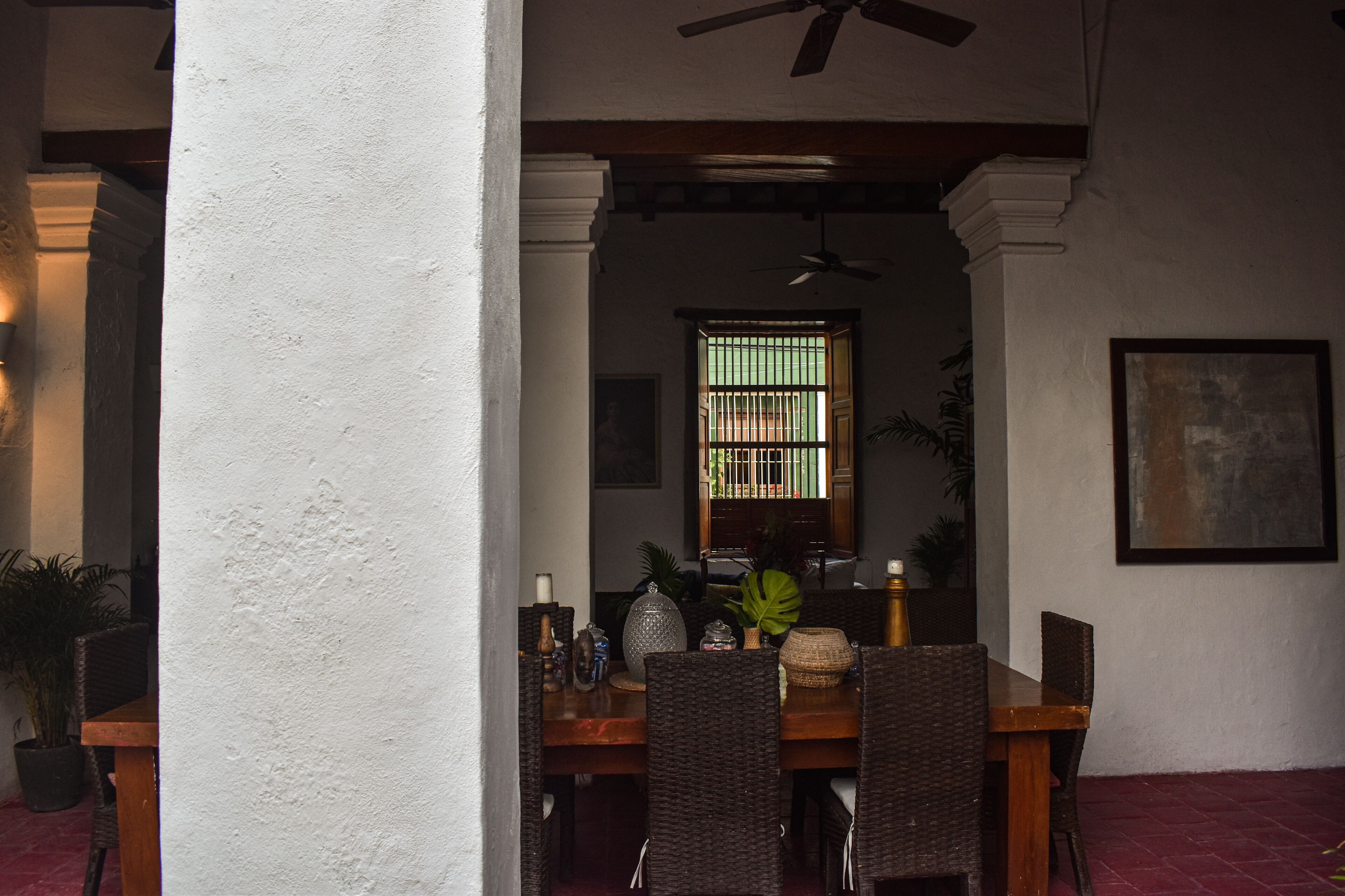 A dining area with a wooden table and wicker chairs, a ceiling fan, and a window with bars.