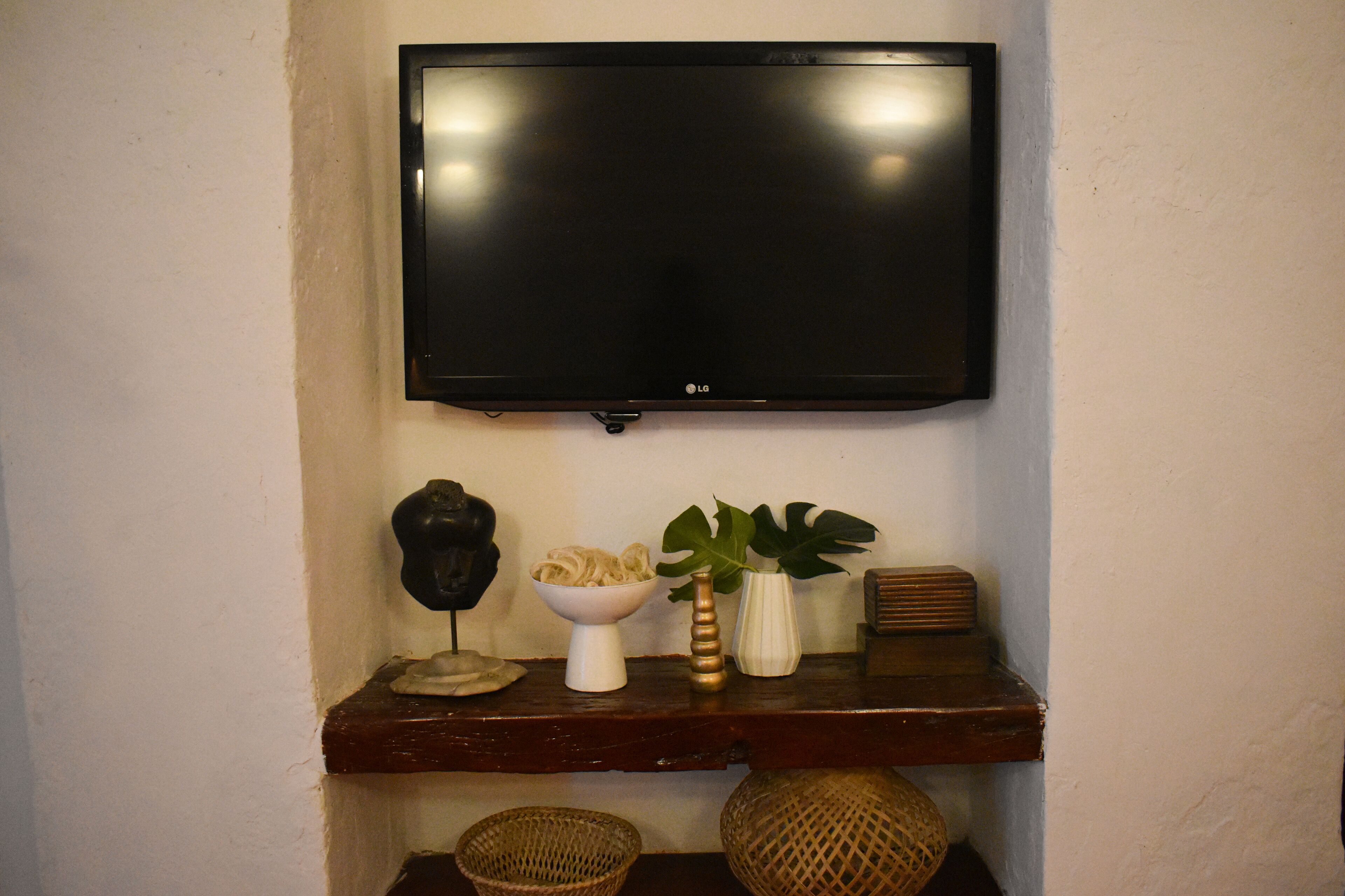 Un televisor de pantalla plana montado en la pared sobre un estante de madera con objetos decorativos.
