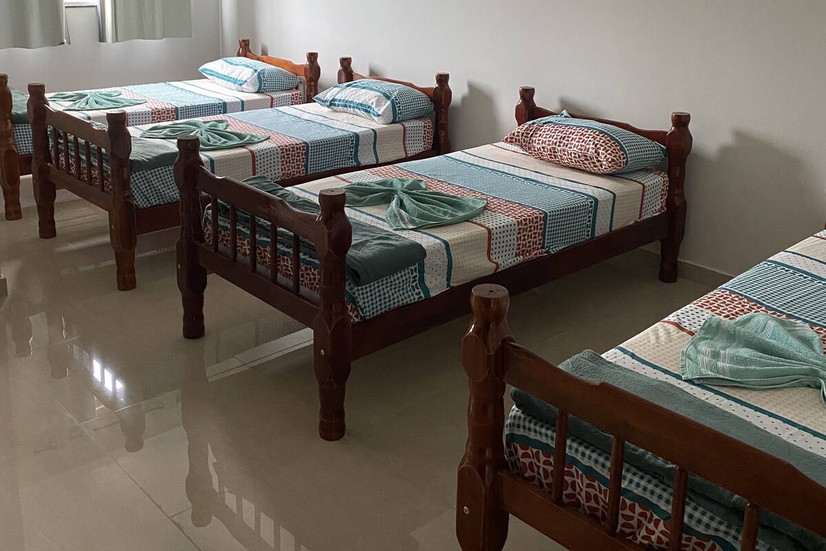 Ein Hotelzimmer mit drei hölzernen Betten, jeweils mit gemusterten Bettbezügen.