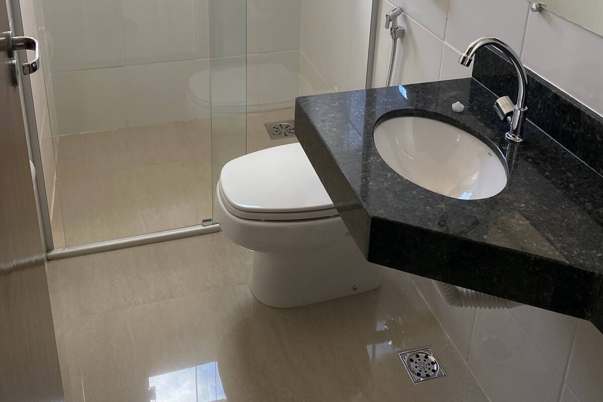 Ein modernes Badezimmer mit einer gläsernen Duschkabine, einer weißen Toilette und einem schwarzen Marmorwaschbecken.