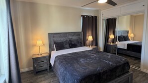 Une chambre à coucher avec un lit, des tables de chevet, un ventilateur de plafond et un miroir.