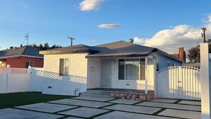 Une propriété résidentielle avec une cour clôturée, une petite maison avec un garage et un ciel bleu dégagé.