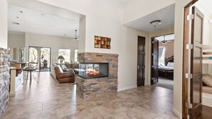 A spacious living area with a stone fireplace, a sofa, and a dining table. - The Genoa House ~ Oasis in the Hills (Fountain Hills)