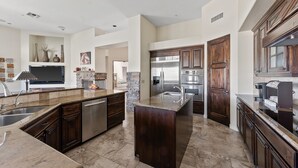 A spacious kitchen with a large island, dark wood cabinets, stainless steel appliances, and a stone accent wall. - The Genoa House ~ Oasis in the Hills (Fountain Hills)