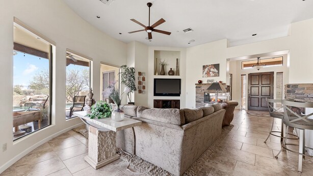 A spacious living area with a large beige sectional sofa, a stone fireplace, a ceiling fan, and a TV mounted on the wall. - The Genoa House ~ Oasis in the Hills (Fountain Hills)