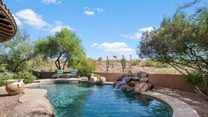 A circular pool with a clear blue center, surrounded by rocks and desert vegetation. - The Genoa House ~ Oasis in the Hills (Fountain Hills)