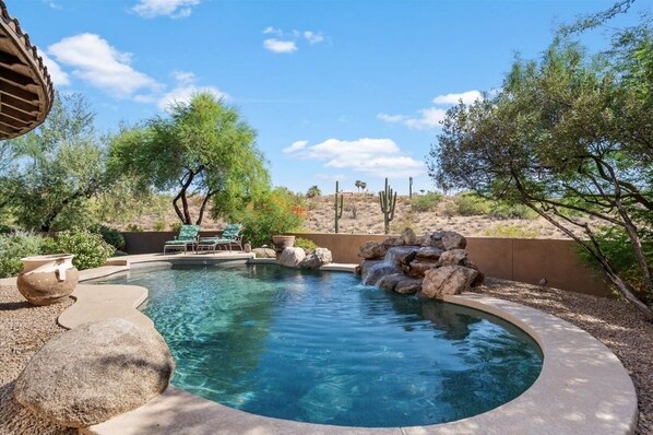 Relax by the serene pool surrounded by desert vegetation and a small waterfall.