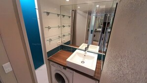 Une petite salle de bain équipée d’un lave-linge, d’un lavabo et d’un miroir.