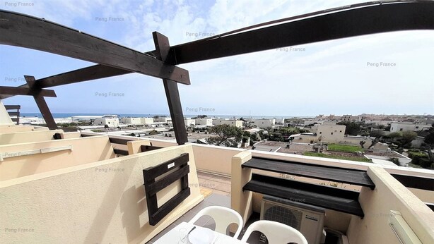 Une terrasse sur le toit, avec une table dressée pour le dîner, offrant une vue sur un quartier résidentiel et la mer.